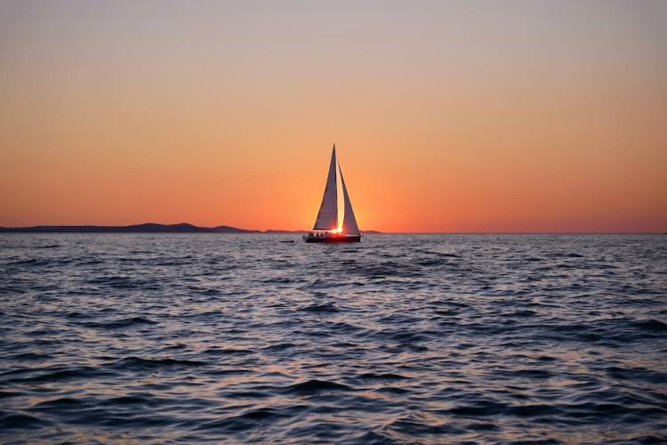 Sailboat in the middle of the ocean during sunset